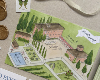 Watercolor map of an Italy wedding venue with venue details on paper and various wedding stationery supplies on a textured surface