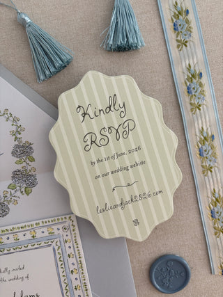 Green striped and scalloped RSVP card for wedding invitation suite with wedding stationery details surrounding it on a textured surface